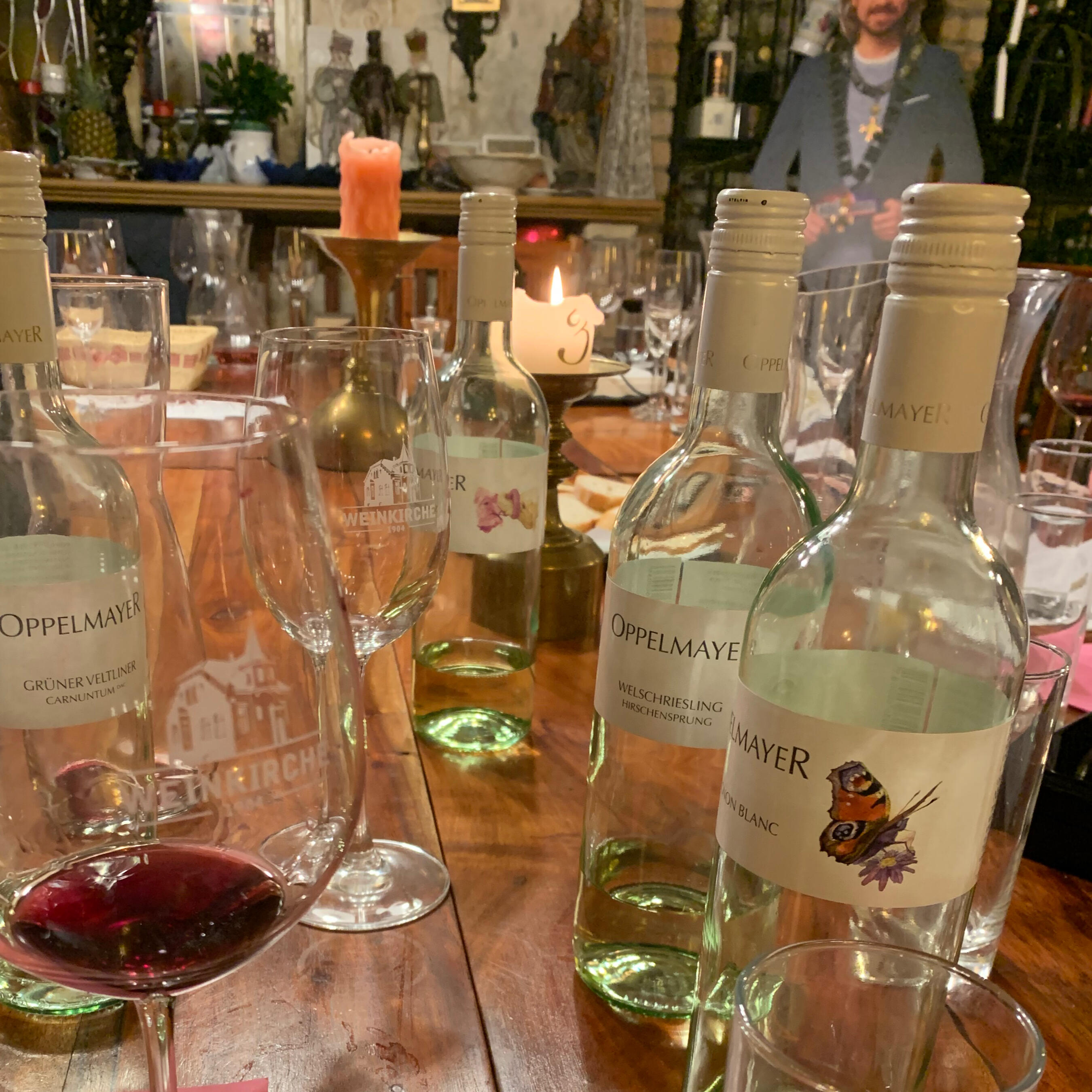 Weinverkostung in der Weinkirche Hainburg: Mehrere Flaschen Oppelmayer-Wein und ein Glas Rotwein auf einem Holztisch bei Kerzenschein.